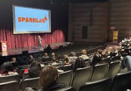  Auditorium seating with speaker on stage, SparkLab logo on projector